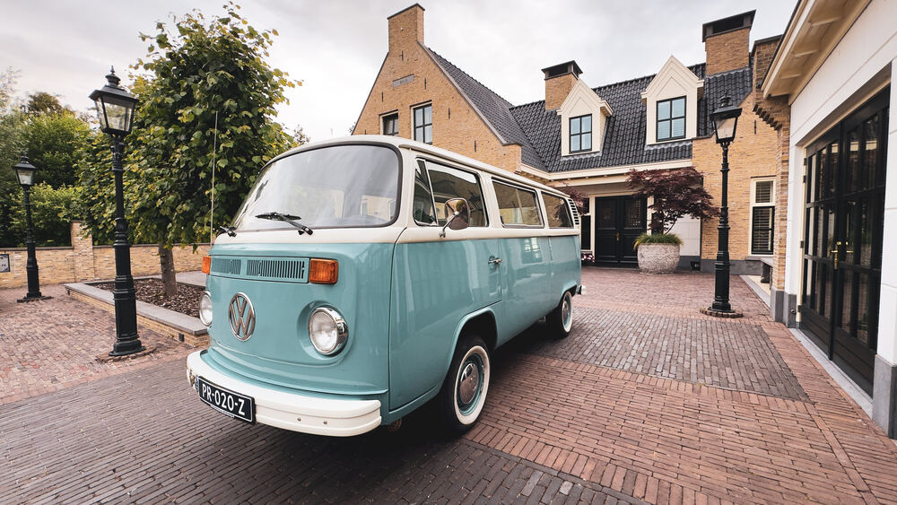 De klassieke VW-bus schuin van voren, naast een gietijzeren straatlantaarn en bomen.