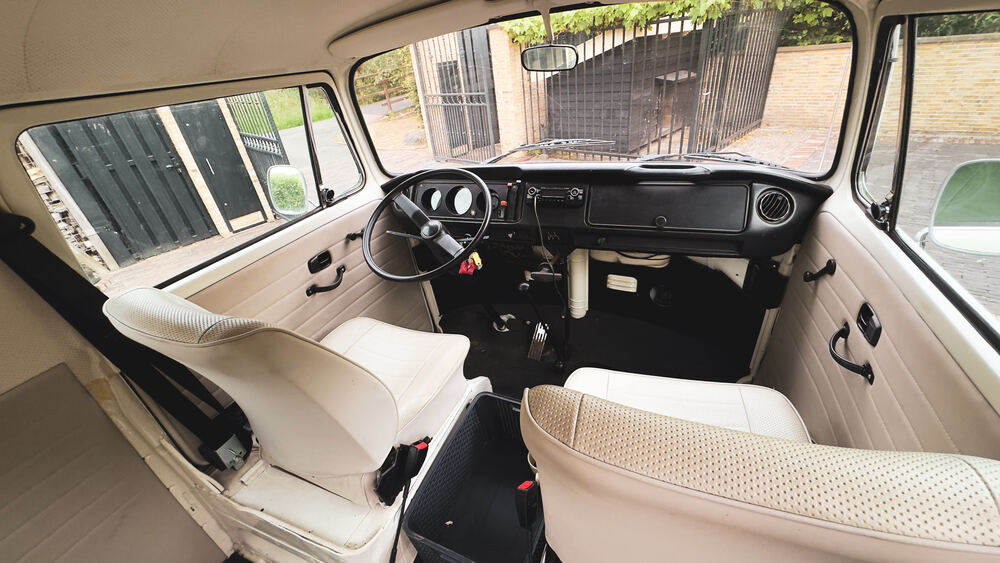 Het crèmekleurige interieur van de VW-bus met dashboard, stuur en bankstoelen.
