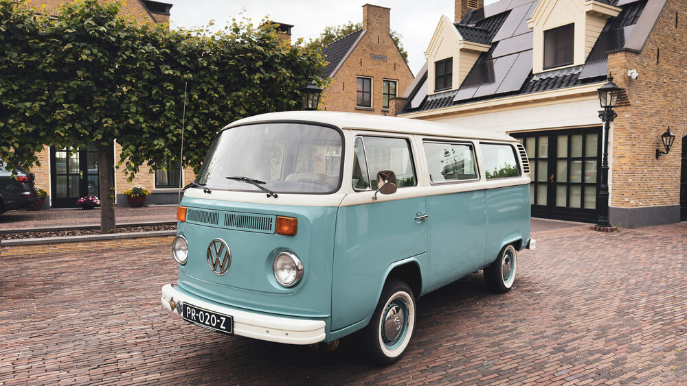 Zeegroen-met-crème Volkswagen T2 uit 1978, schuin van voren op de klinkers voor een Nederlands herenhuis.